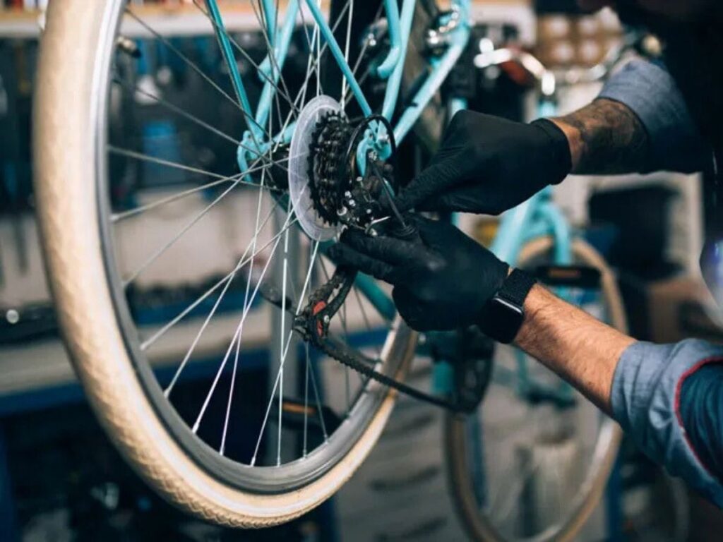 Técnico ajusta transmisión y cadena de bicicleta con guantes, realizando mantenimiento preventivo en taller.